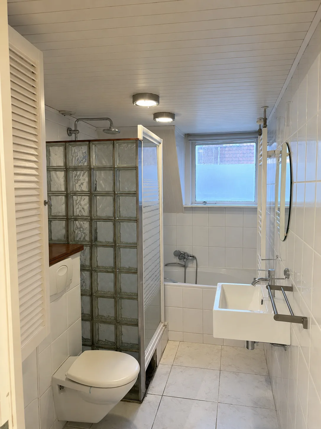 Een badkamer in Rotterdam voor de renovatie, met glazen bouwstenen rond de douche en een houten plafond
