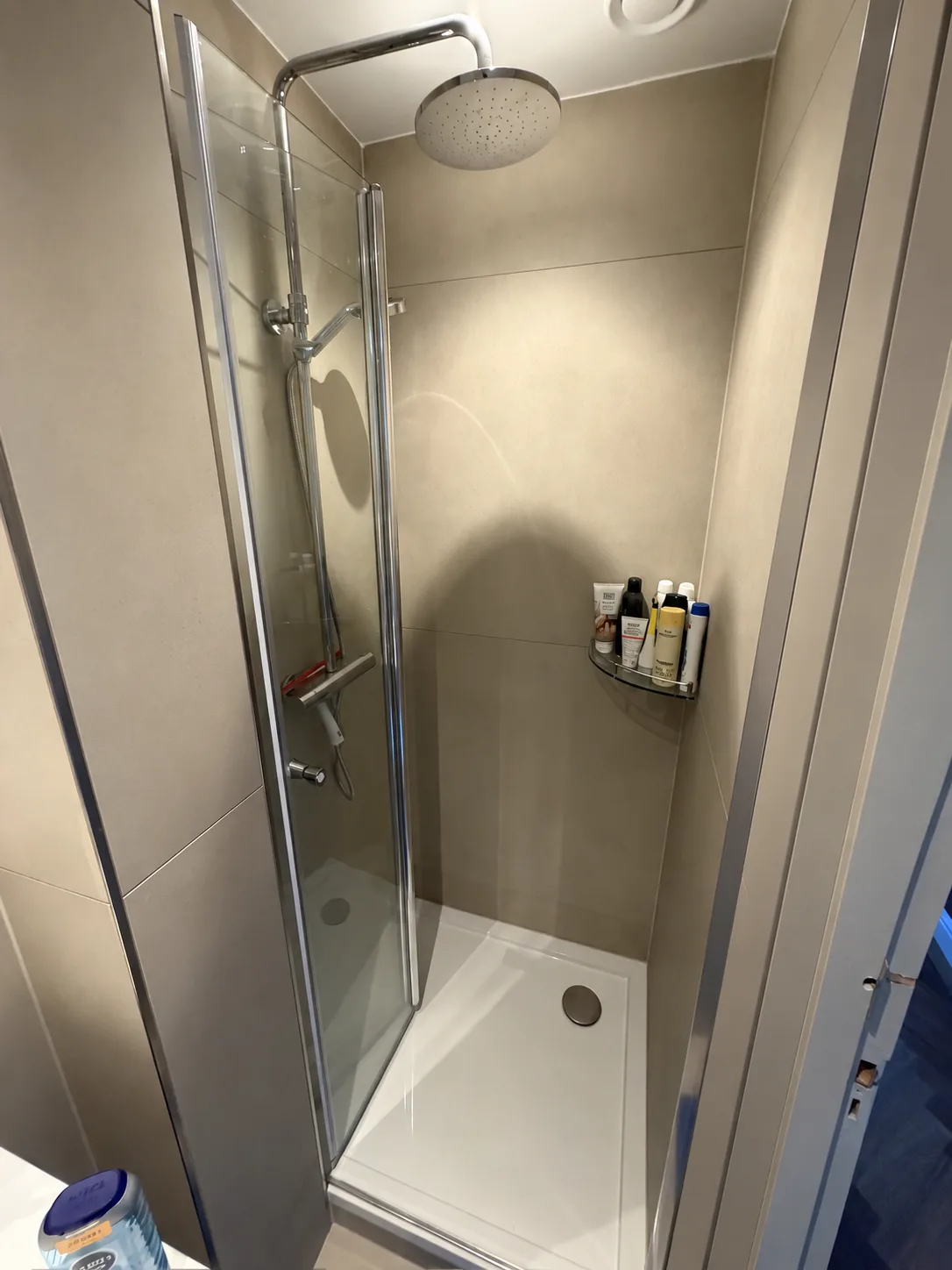 Dezelfde douche na de renovatie, met een lage douchebak, een regendouche en tegelwerk in één tint
