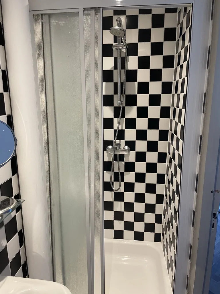 De douche voor de renovatie, met schuifdeuren en zwart-wit tegelwerk