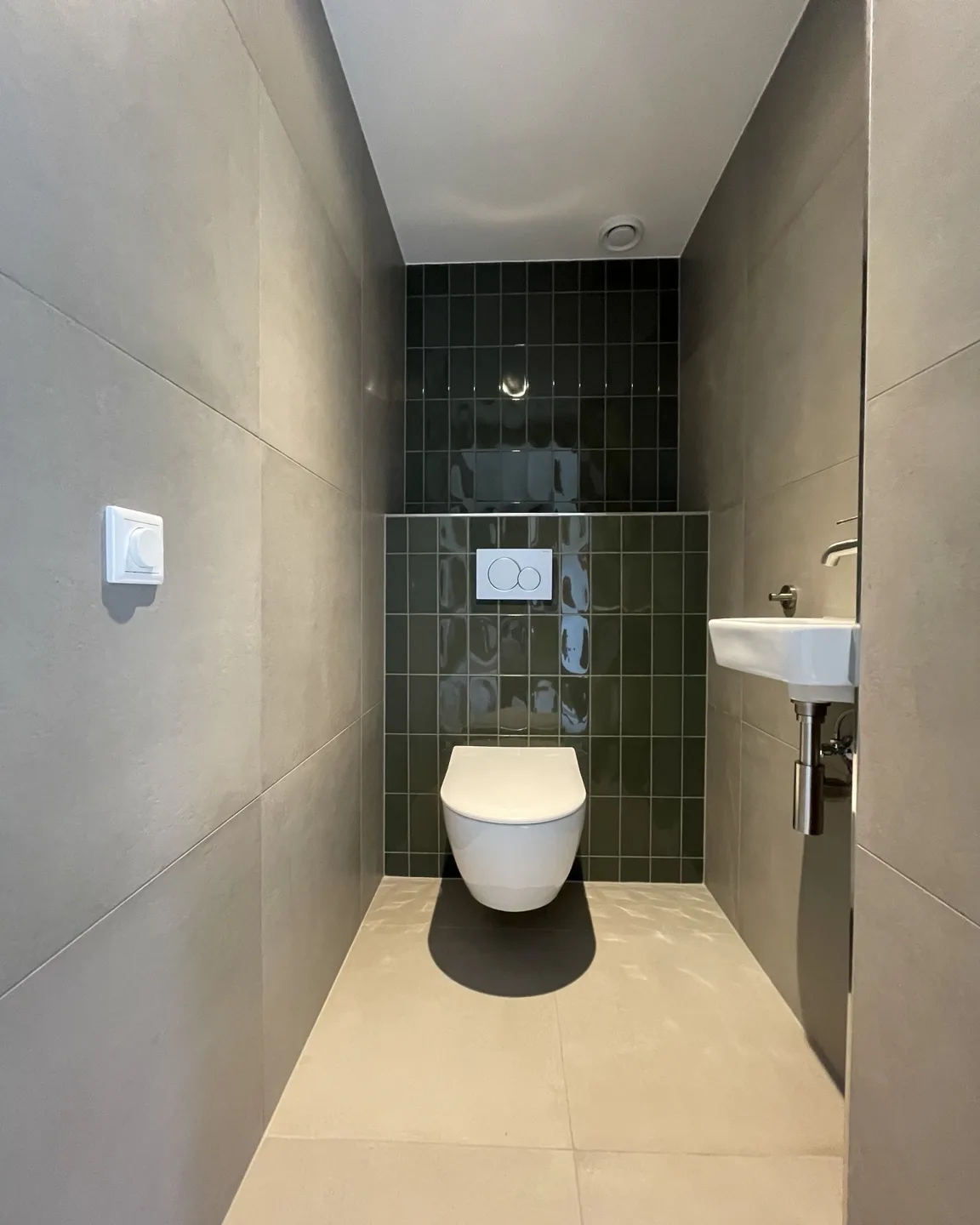 Vernieuwd toilet met donkergroen tegelwerk en een zwevend closet
