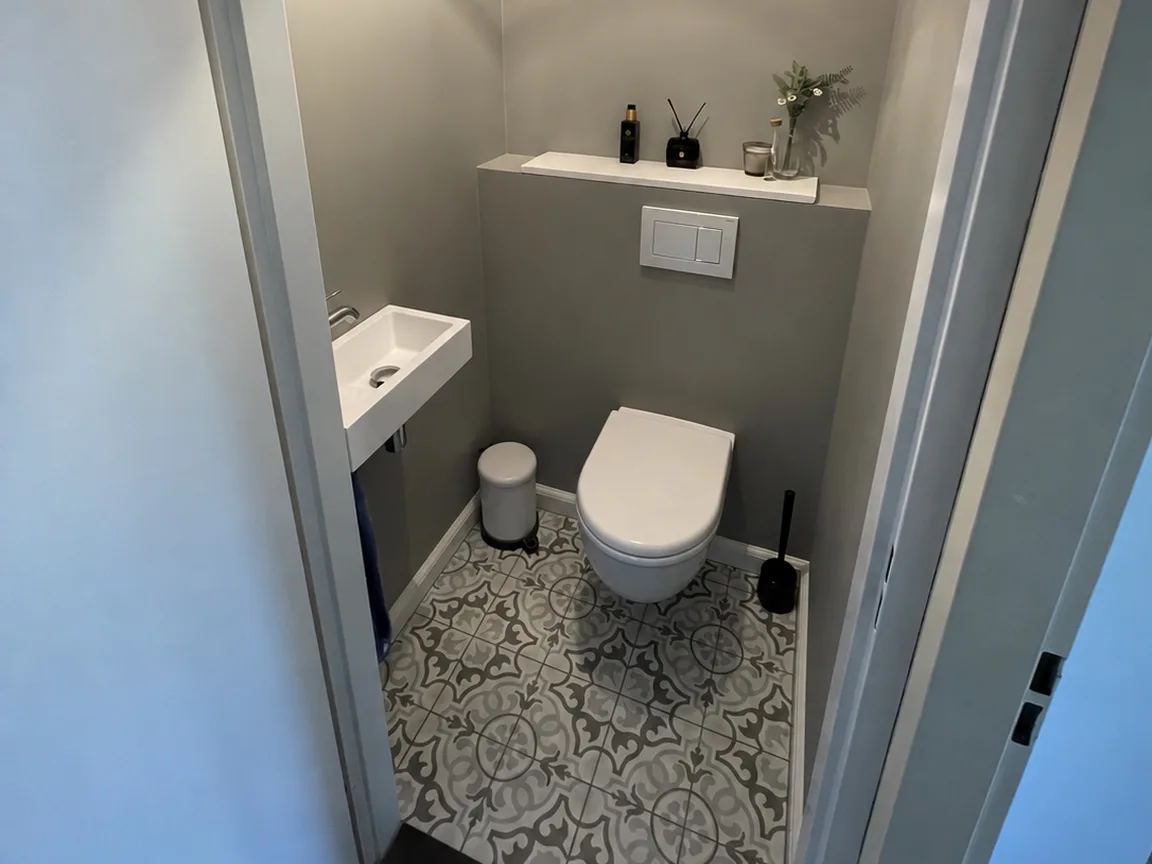 Hetzelfde toilet na de renovatie, met een patroonvloer en een zwevend closet