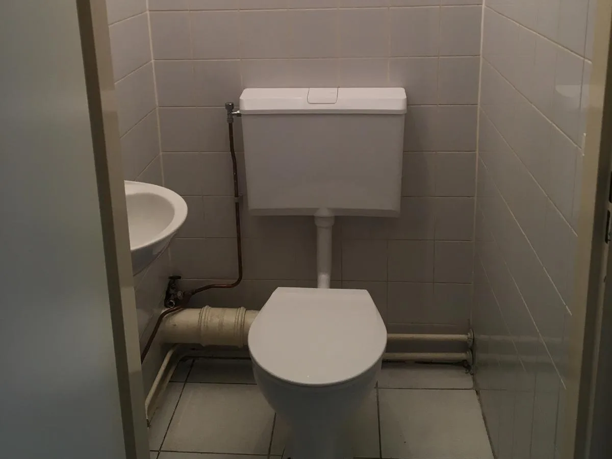 Het oorspronkelijke toilet met een staand reservoir en leidingwerk in het zicht