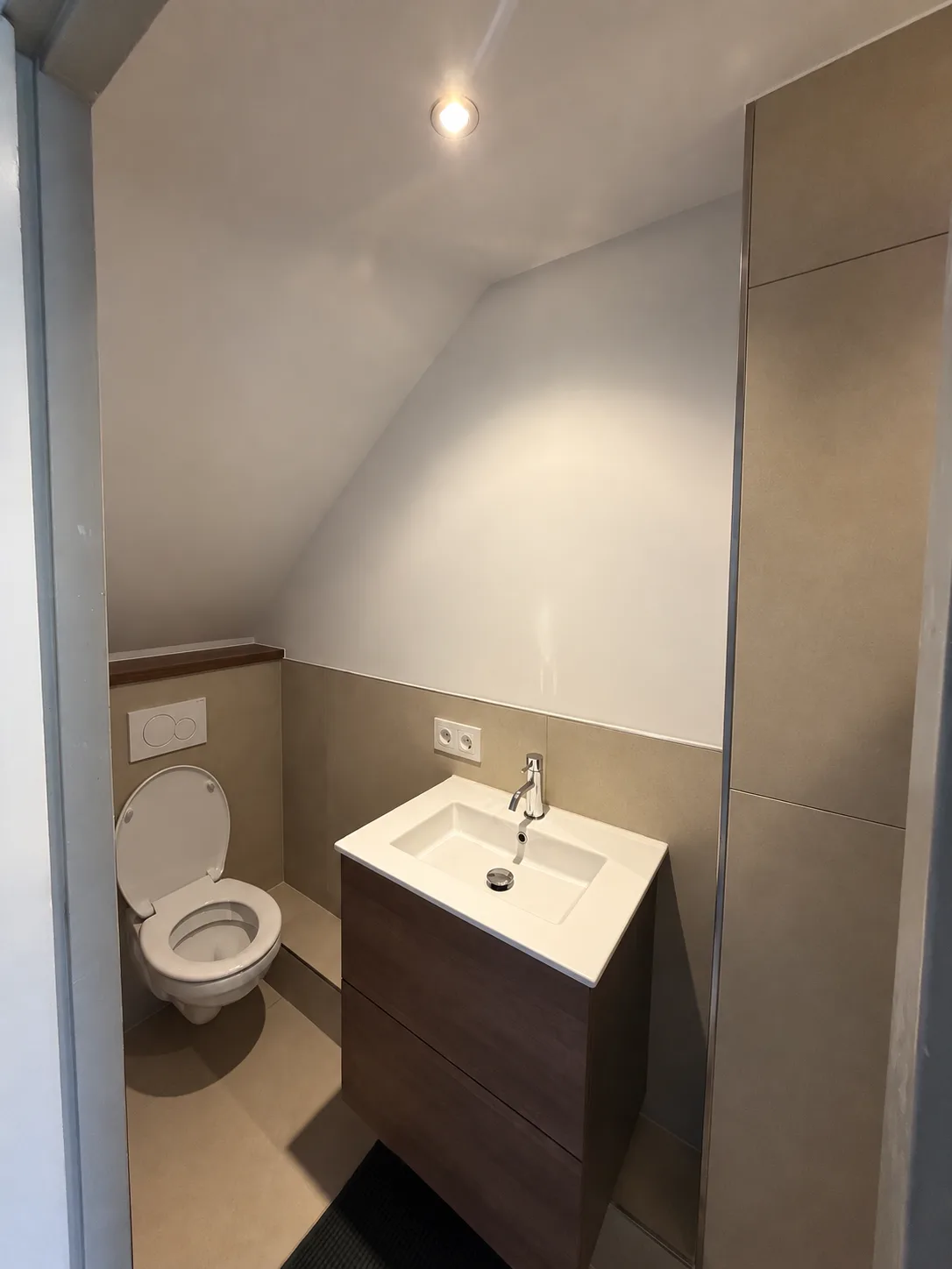 Hetzelfde toilet na de renovatie, met een zwevend closet en een wastafelmeubel onder het schuine dak