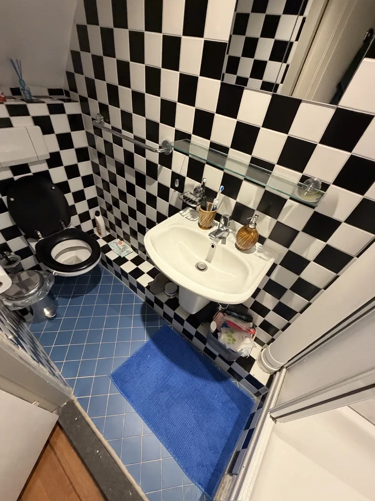 Het toilet met wasbak voor de renovatie, met zwart-witte wandtegels en een blauwe vloer