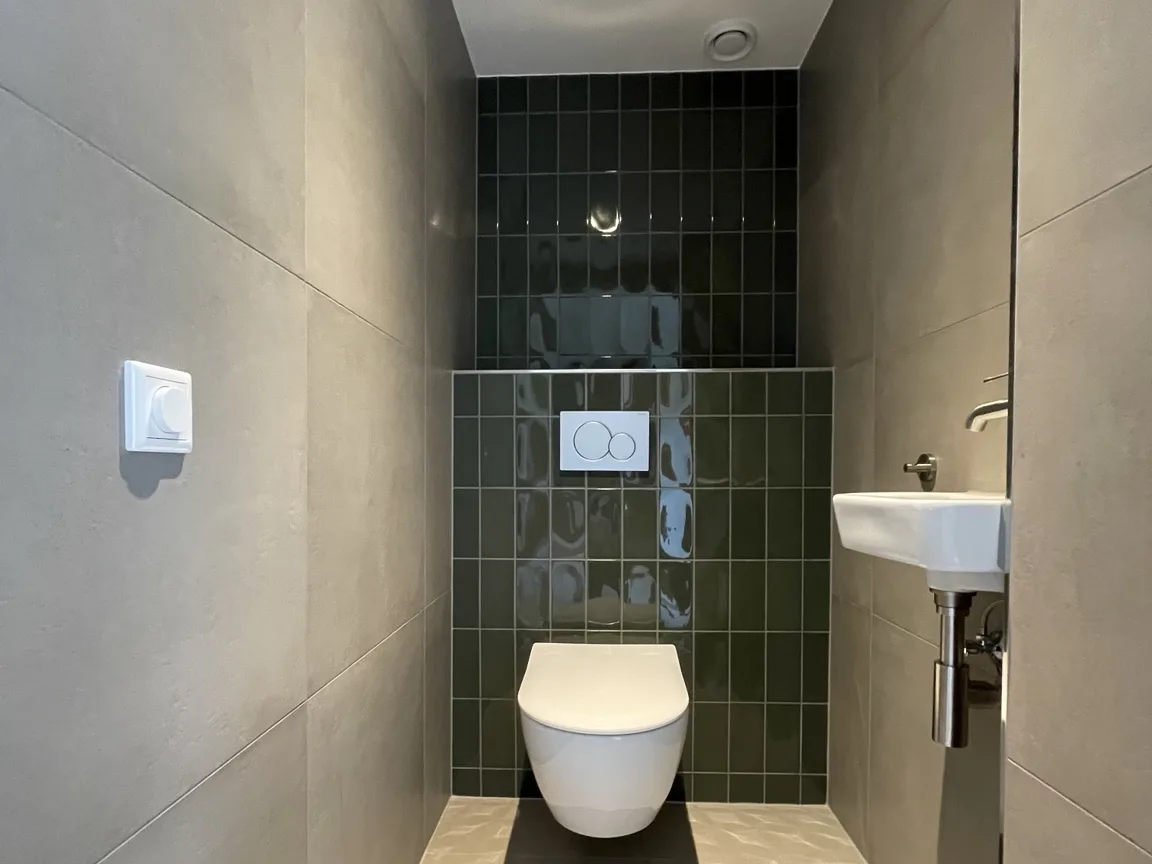 Hetzelfde toilet na afwerking, met donkergroen tegelwerk en een zwevend closet