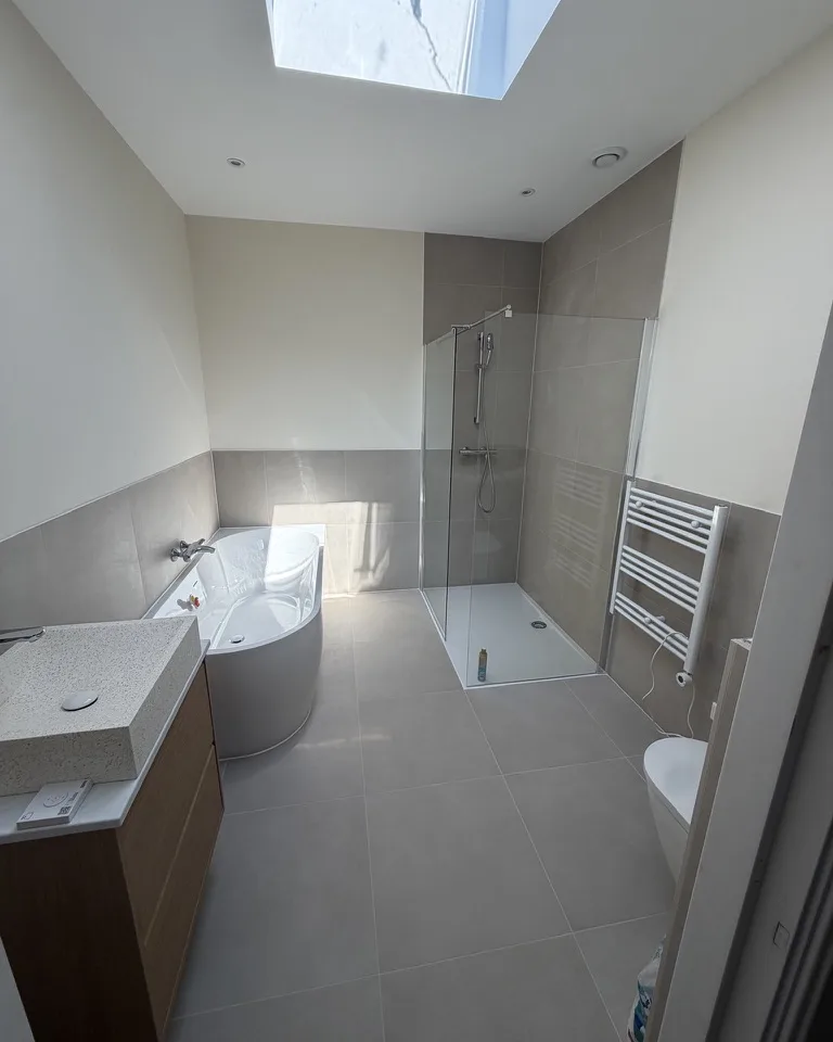 Badkamer onder een dakraam, met een hoekbad en een inloopdouche