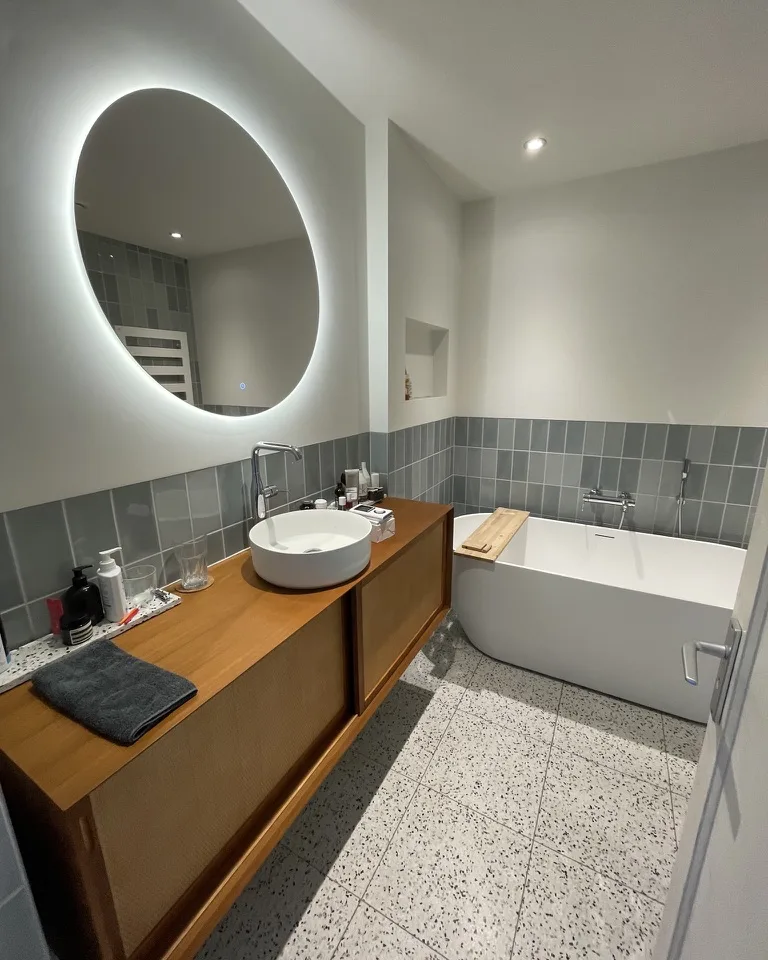 Badkamer met een houten meubel, twee opzetkommen en een bad langs de wand