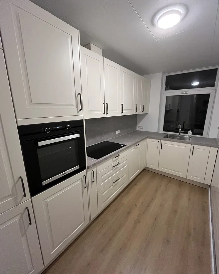 Keuken met witte kastfronten, een inbouwoven en een houten vloer