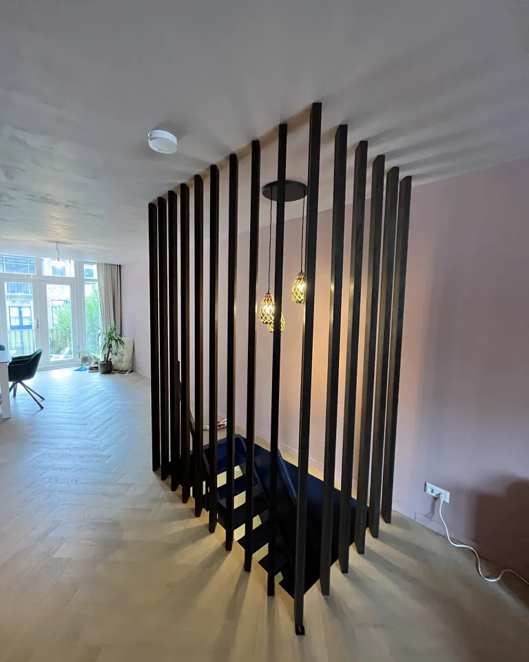 Woonruimte met een zwarte lattenwand als scheiding, op een visgraatvloer