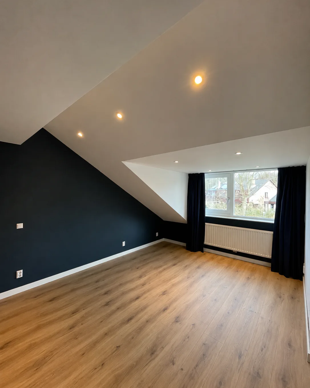 Slaapkamer onder een schuin dak, met een donkerblauwe wand