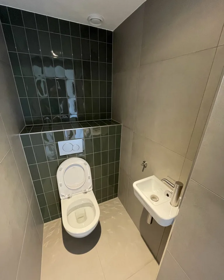 Toilet met donkergroen tegelwerk en een fonteintje