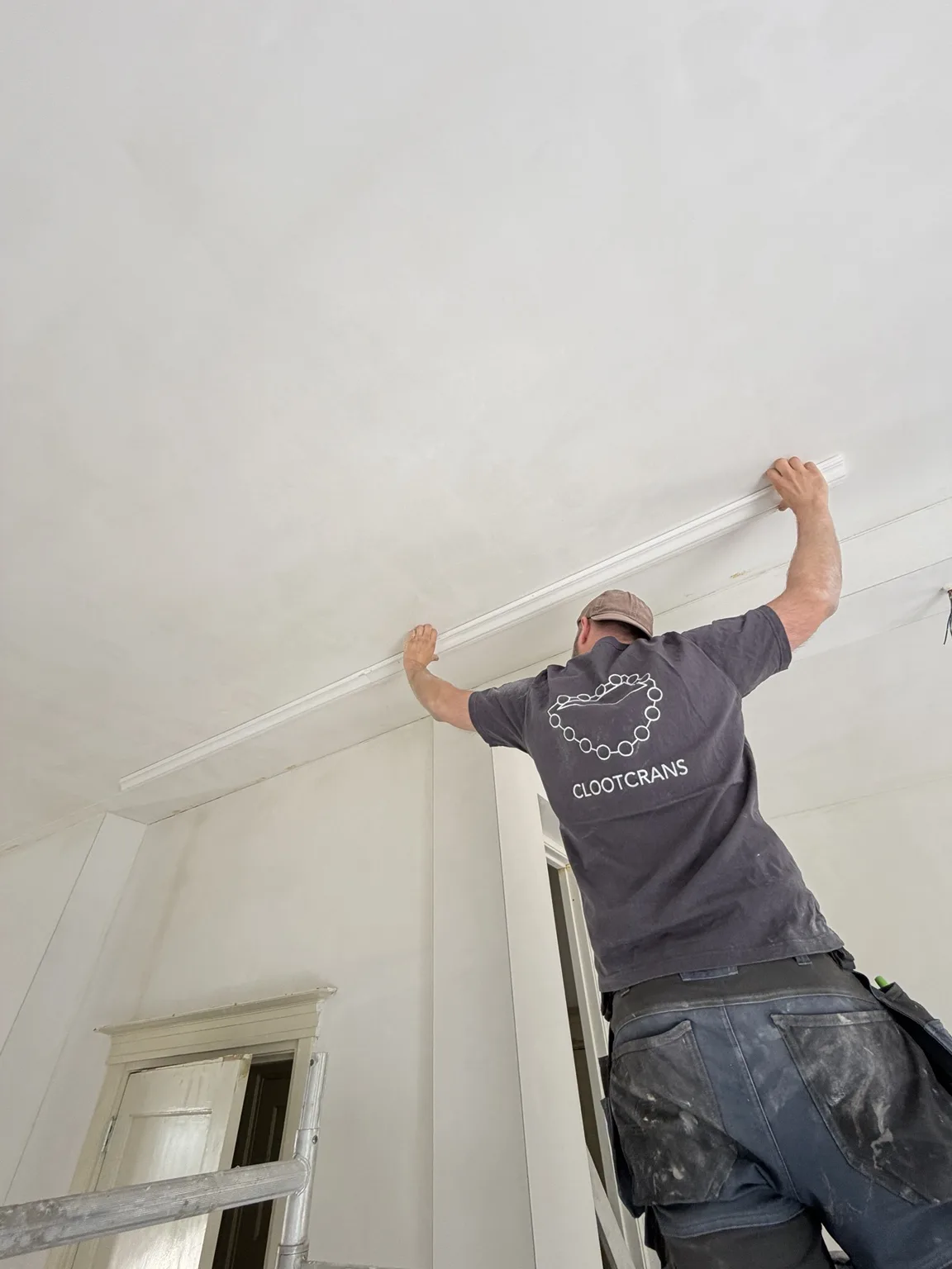 Vakman van Clootcrans plaatst een sierlijst tegen het plafond tijdens een renovatie in Rotterdam